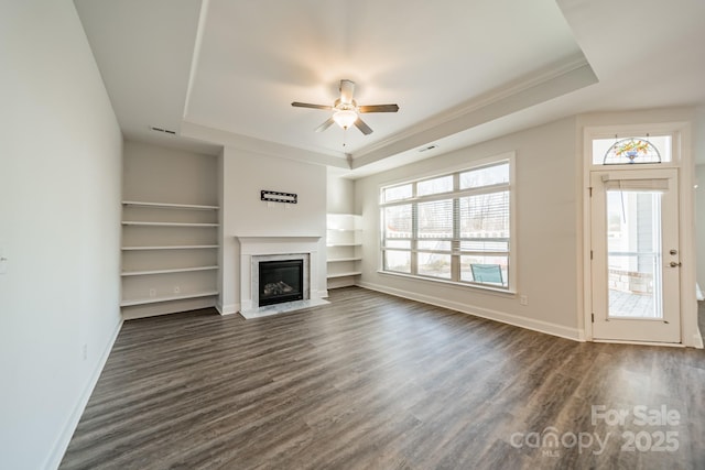 unfurnished living room with baseboards, a raised ceiling, and dark wood-type flooring