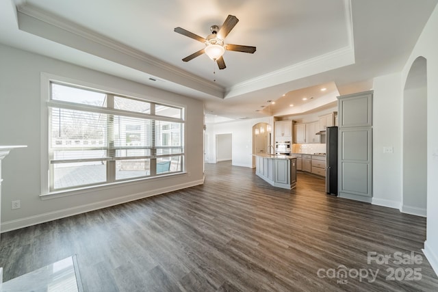 unfurnished living room with a tray ceiling, arched walkways, dark wood finished floors, and crown molding