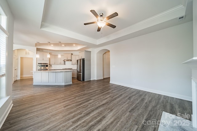 unfurnished living room featuring a raised ceiling, arched walkways, and dark wood-style flooring