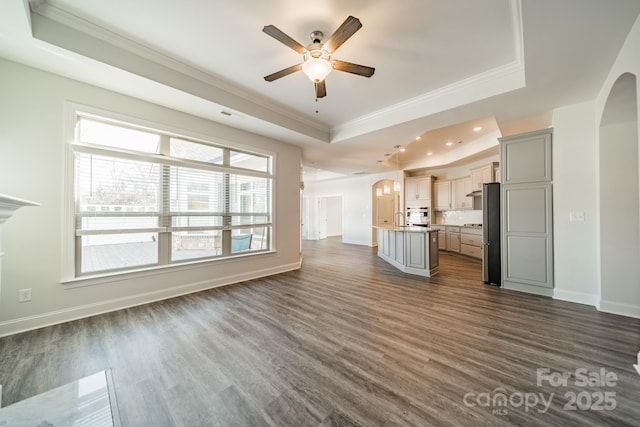 unfurnished living room with a tray ceiling, arched walkways, and dark wood finished floors