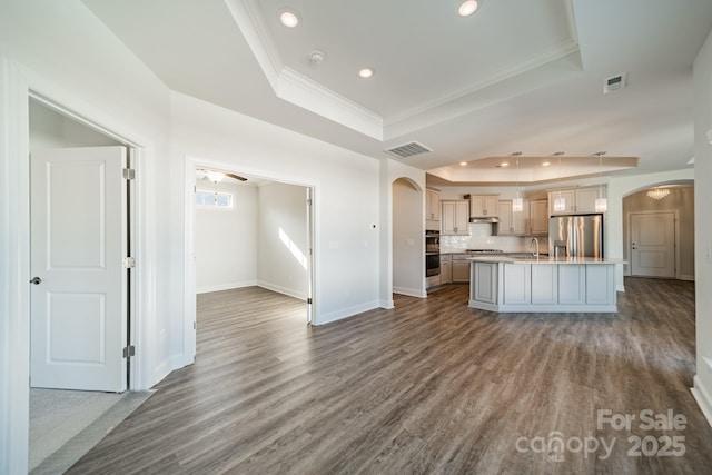 kitchen with a raised ceiling, arched walkways, stainless steel fridge, and dark wood-type flooring