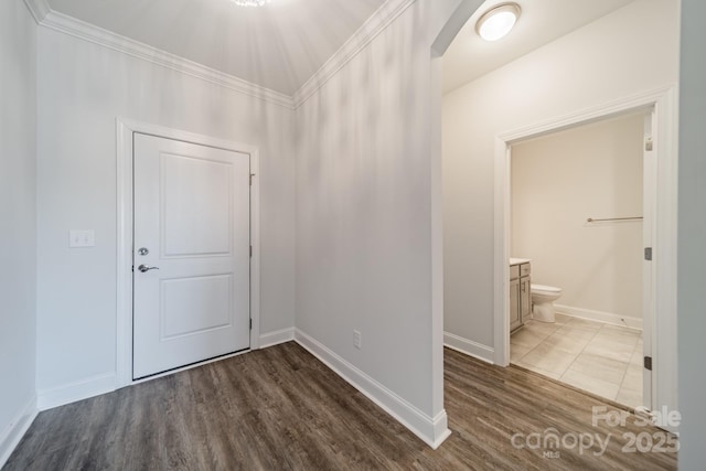 foyer entrance featuring crown molding, wood finished floors, arched walkways, and baseboards