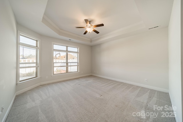 empty room with visible vents, baseboards, a tray ceiling, ornamental molding, and light carpet