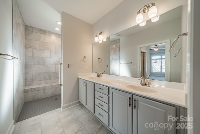 full bath featuring a ceiling fan, baseboards, tiled shower, double vanity, and a sink