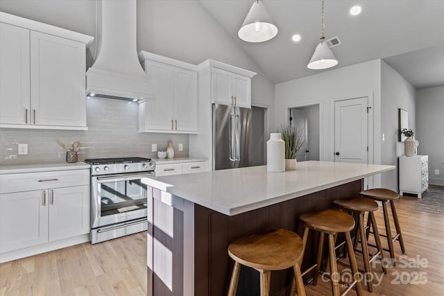 kitchen featuring visible vents, a kitchen island, vaulted ceiling, appliances with stainless steel finishes, and custom exhaust hood