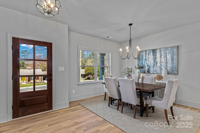 dining area with a chandelier, light wood-type flooring, healthy amount of natural light, and baseboards