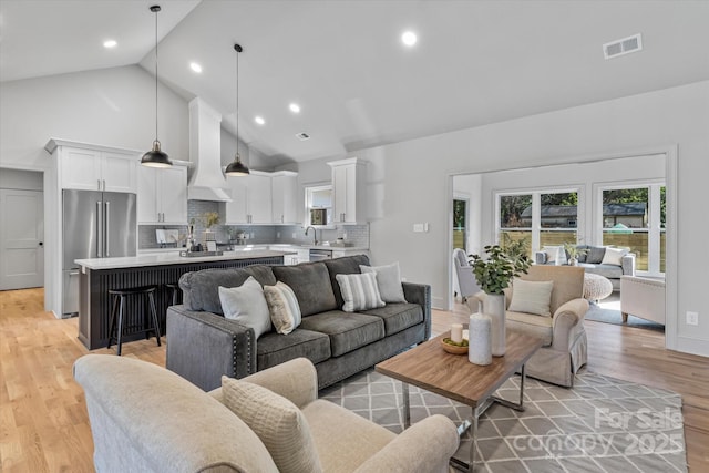 living area featuring high vaulted ceiling, light wood finished floors, recessed lighting, and baseboards