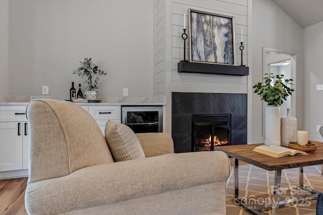 living area with a high end fireplace, beverage cooler, light wood-type flooring, and lofted ceiling