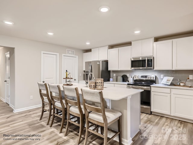 kitchen featuring light wood-style floors, tasteful backsplash, appliances with stainless steel finishes, and a kitchen island with sink