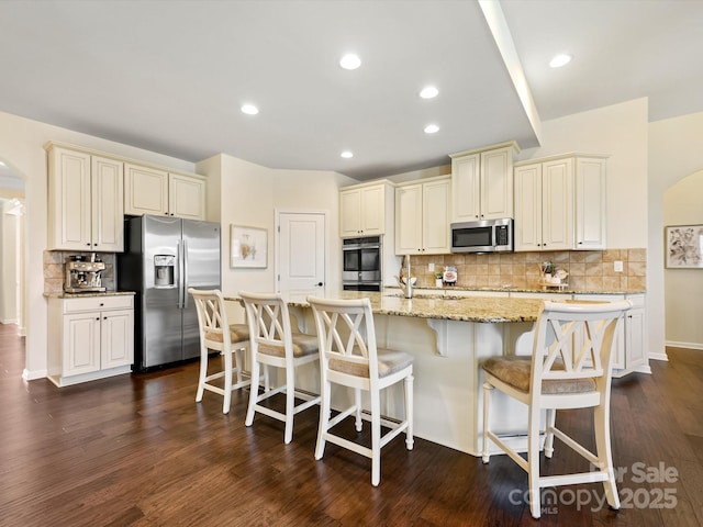 kitchen featuring light stone countertops, stainless steel appliances, decorative backsplash, dark wood-type flooring, and cream cabinets