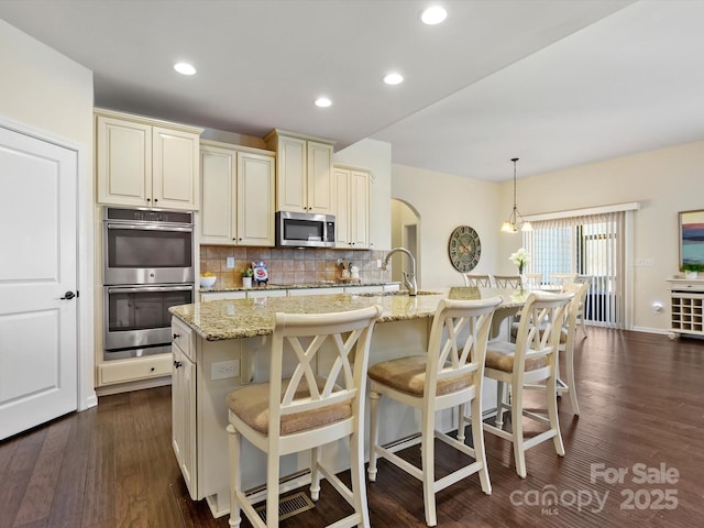 kitchen with light stone counters, decorative backsplash, appliances with stainless steel finishes, dark wood-style floors, and a sink