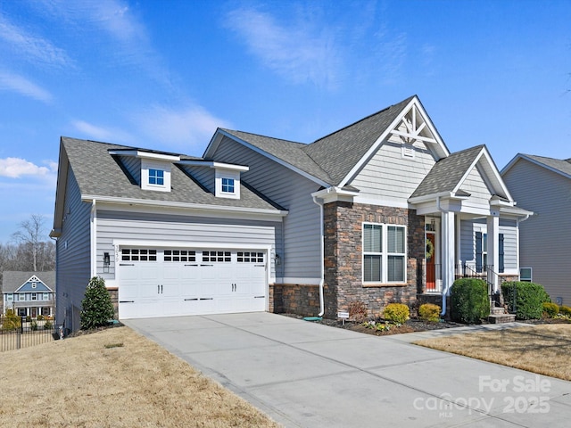 craftsman-style house featuring a shingled roof, fence, driveway, stone siding, and an attached garage