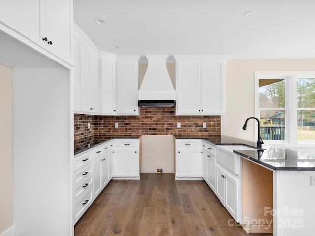 kitchen featuring a peninsula, premium range hood, backsplash, and a sink