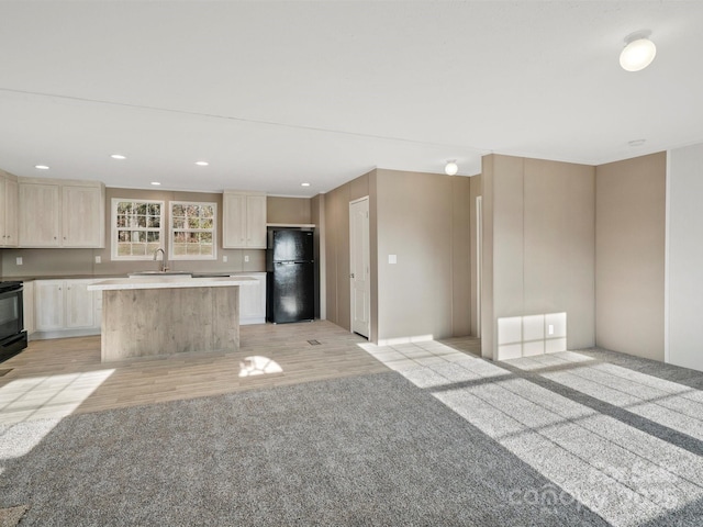 kitchen featuring a center island, light countertops, recessed lighting, freestanding refrigerator, and a sink