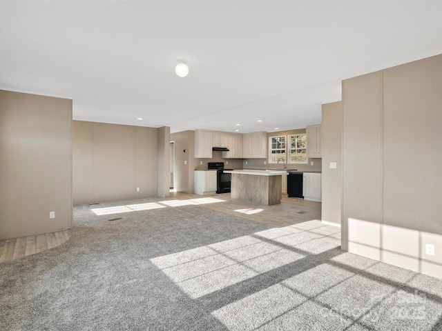 unfurnished living room featuring recessed lighting, light colored carpet, and a sink