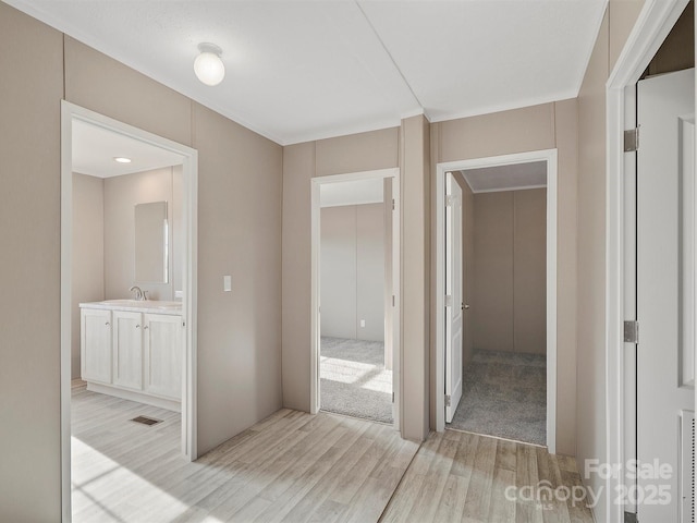 hallway featuring visible vents, light wood-type flooring, and a sink