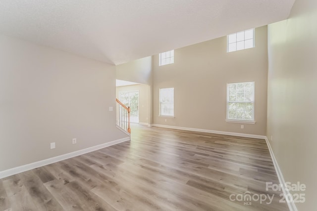 empty room featuring stairway, a textured ceiling, baseboards, and light wood-style floors