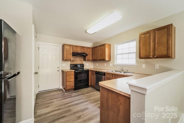 kitchen featuring brown cabinetry, a peninsula, a sink, black appliances, and under cabinet range hood