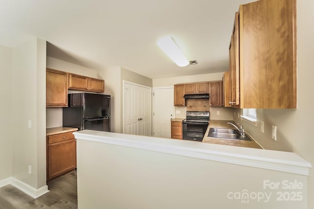 kitchen with a peninsula, electric range, freestanding refrigerator, a sink, and under cabinet range hood