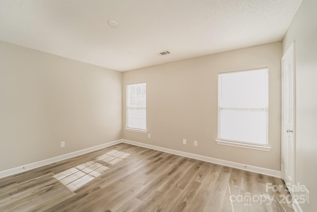 empty room featuring visible vents, light wood-type flooring, and baseboards