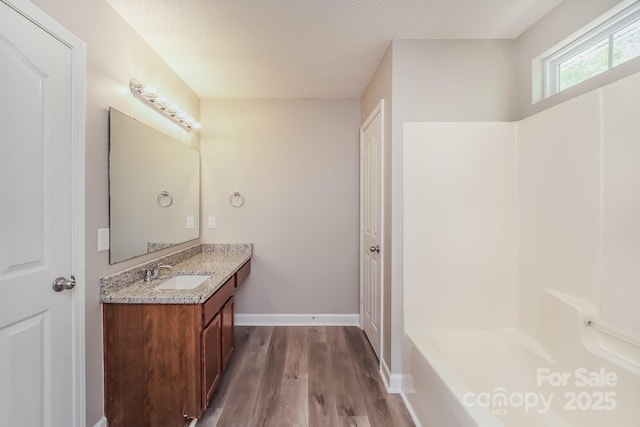 bathroom with a washtub, vanity, baseboards, and wood finished floors