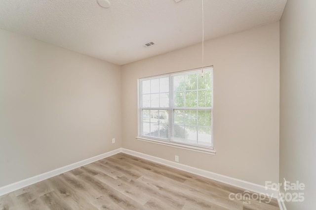 empty room with attic access, baseboards, light wood finished floors, and a textured ceiling