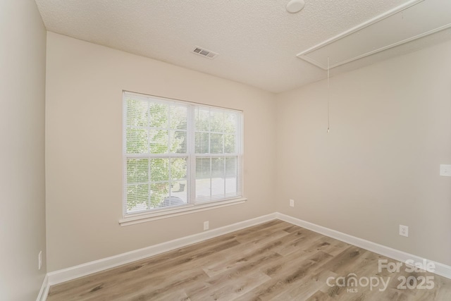 spare room with visible vents, attic access, light wood-type flooring, and baseboards