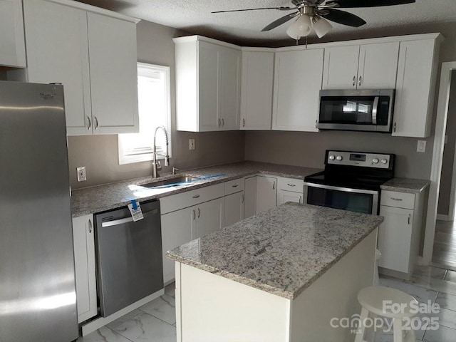 kitchen with a sink, stainless steel appliances, white cabinets, a textured ceiling, and marble finish floor