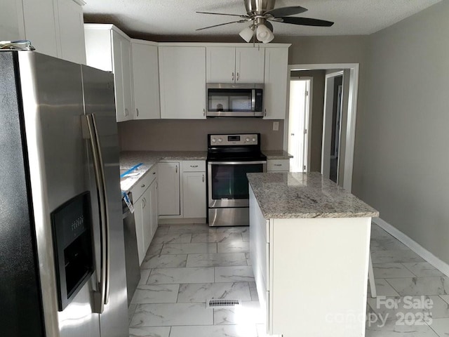 kitchen featuring a center island, baseboards, appliances with stainless steel finishes, marble finish floor, and a textured ceiling