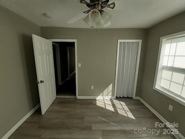 unfurnished bedroom featuring wood finished floors, baseboards, a closet, and a textured ceiling