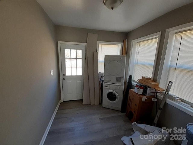 laundry area featuring baseboards, stacked washer and clothes dryer, wood finished floors, and laundry area