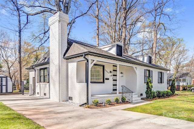 view of front of home featuring brick siding, a front lawn, covered porch, a chimney, and driveway