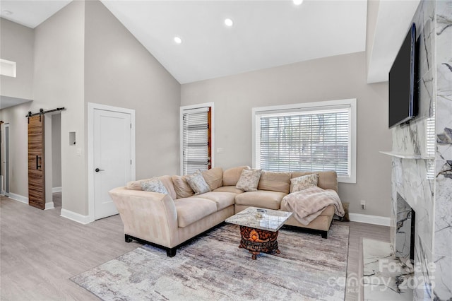 living area with high vaulted ceiling, baseboards, a barn door, and wood finished floors