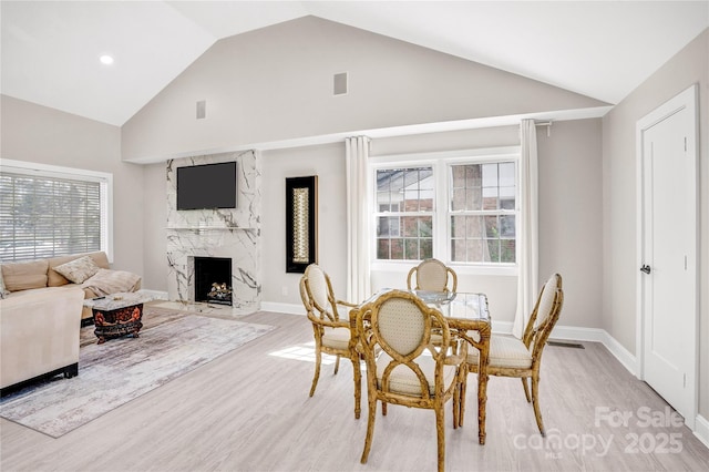dining room featuring a high end fireplace, visible vents, baseboards, light wood-style flooring, and high vaulted ceiling