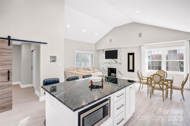 kitchen featuring dark stone countertops, a barn door, a fireplace, white cabinetry, and stainless steel microwave