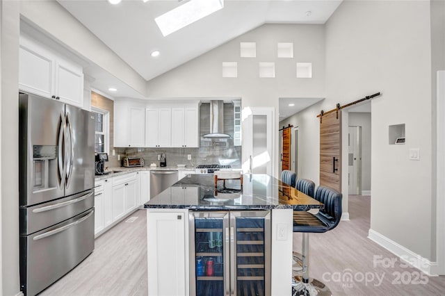 kitchen with a breakfast bar area, beverage cooler, appliances with stainless steel finishes, a barn door, and wall chimney exhaust hood