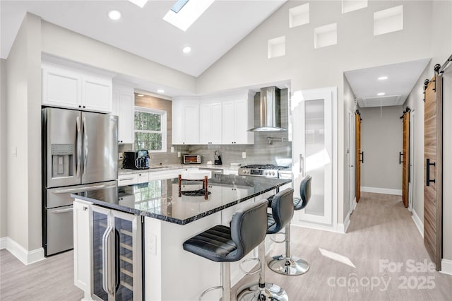 kitchen featuring stainless steel refrigerator with ice dispenser, wine cooler, a breakfast bar area, wall chimney exhaust hood, and white cabinets
