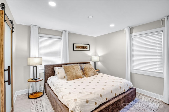 bedroom featuring a barn door, recessed lighting, light wood-style floors, and baseboards