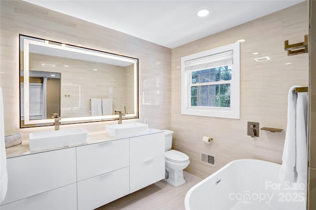 full bath with visible vents, a freestanding tub, tile walls, and a sink