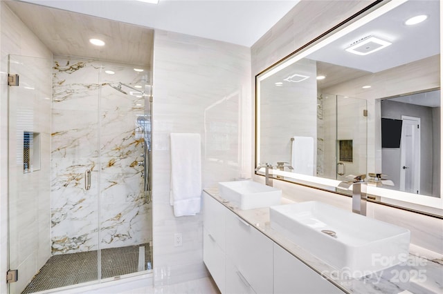 full bath with a marble finish shower, recessed lighting, double vanity, and a sink