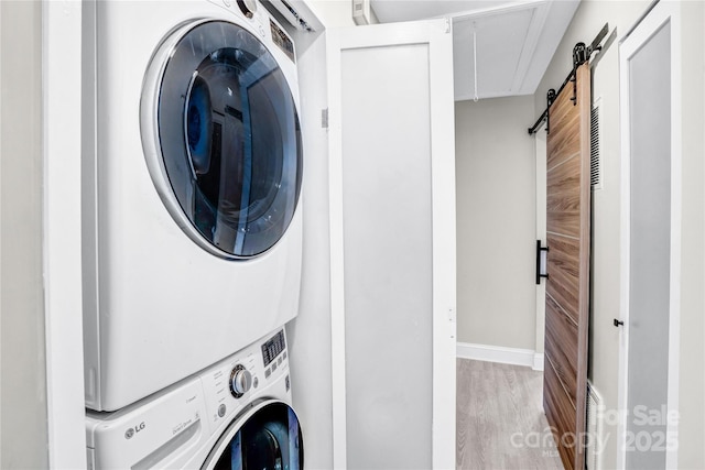 washroom with wood finished floors, baseboards, laundry area, a barn door, and stacked washer / dryer