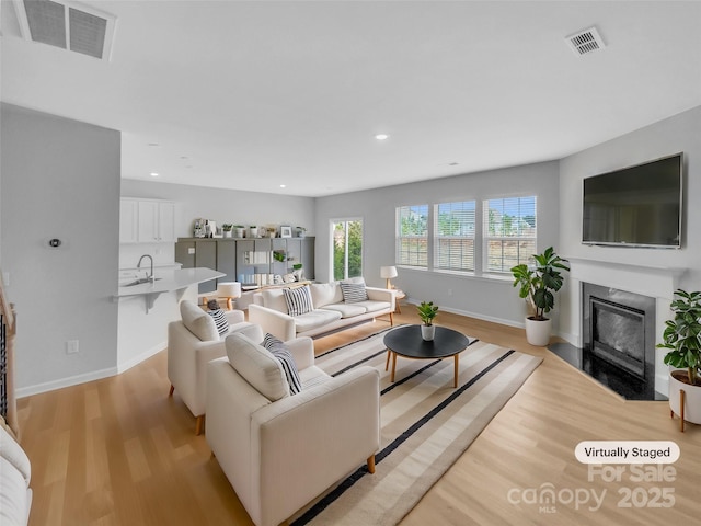 living room featuring a high end fireplace, visible vents, light wood-style flooring, and baseboards