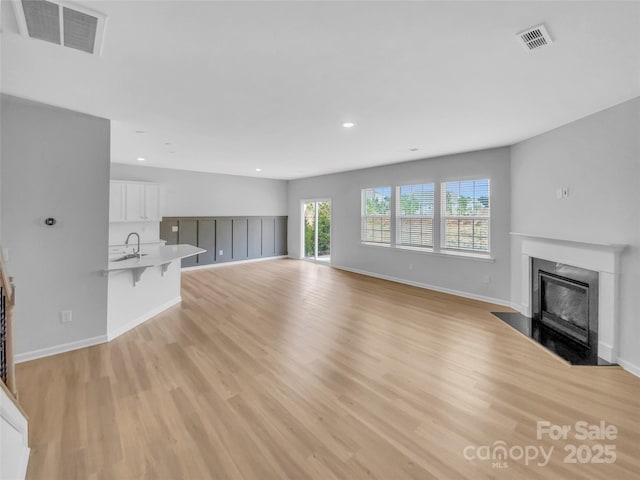 unfurnished living room featuring a high end fireplace, visible vents, baseboards, light wood-type flooring, and a sink