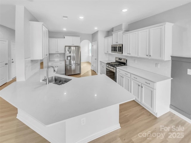 kitchen featuring light wood finished floors, appliances with stainless steel finishes, a peninsula, arched walkways, and a sink