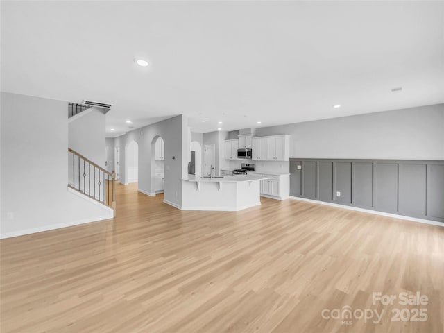 unfurnished living room with recessed lighting, stairway, light wood-style floors, and a sink