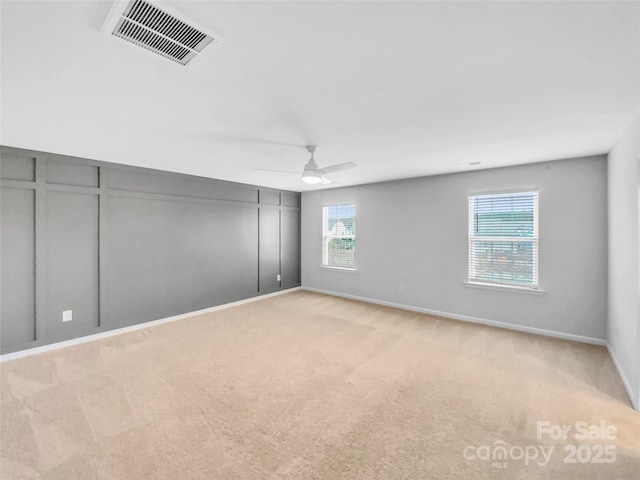 unfurnished room with a wealth of natural light, visible vents, light colored carpet, and ceiling fan