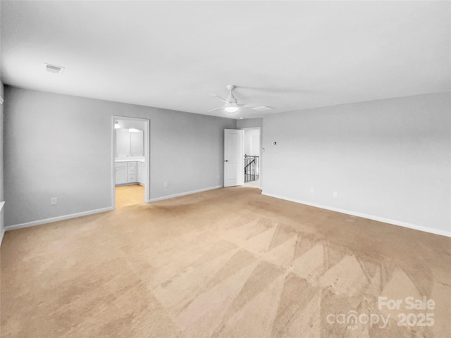 empty room featuring ceiling fan, light colored carpet, visible vents, and baseboards