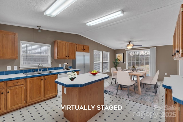 kitchen featuring a sink, built in fridge, lofted ceiling, light floors, and tile counters