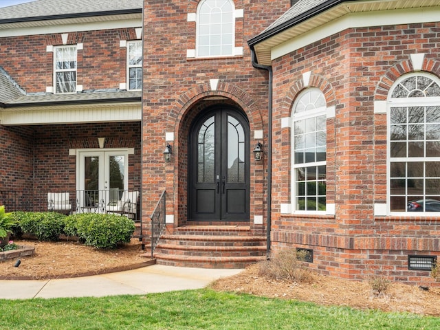 view of exterior entry with french doors, brick siding, and crawl space