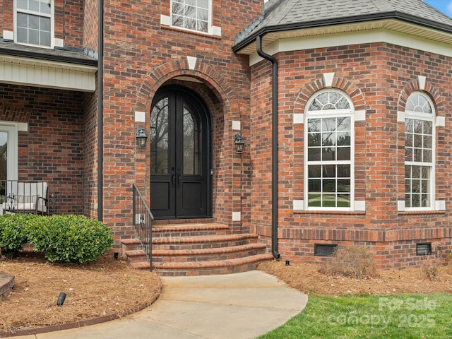 view of exterior entry with crawl space, brick siding, roof with shingles, and french doors